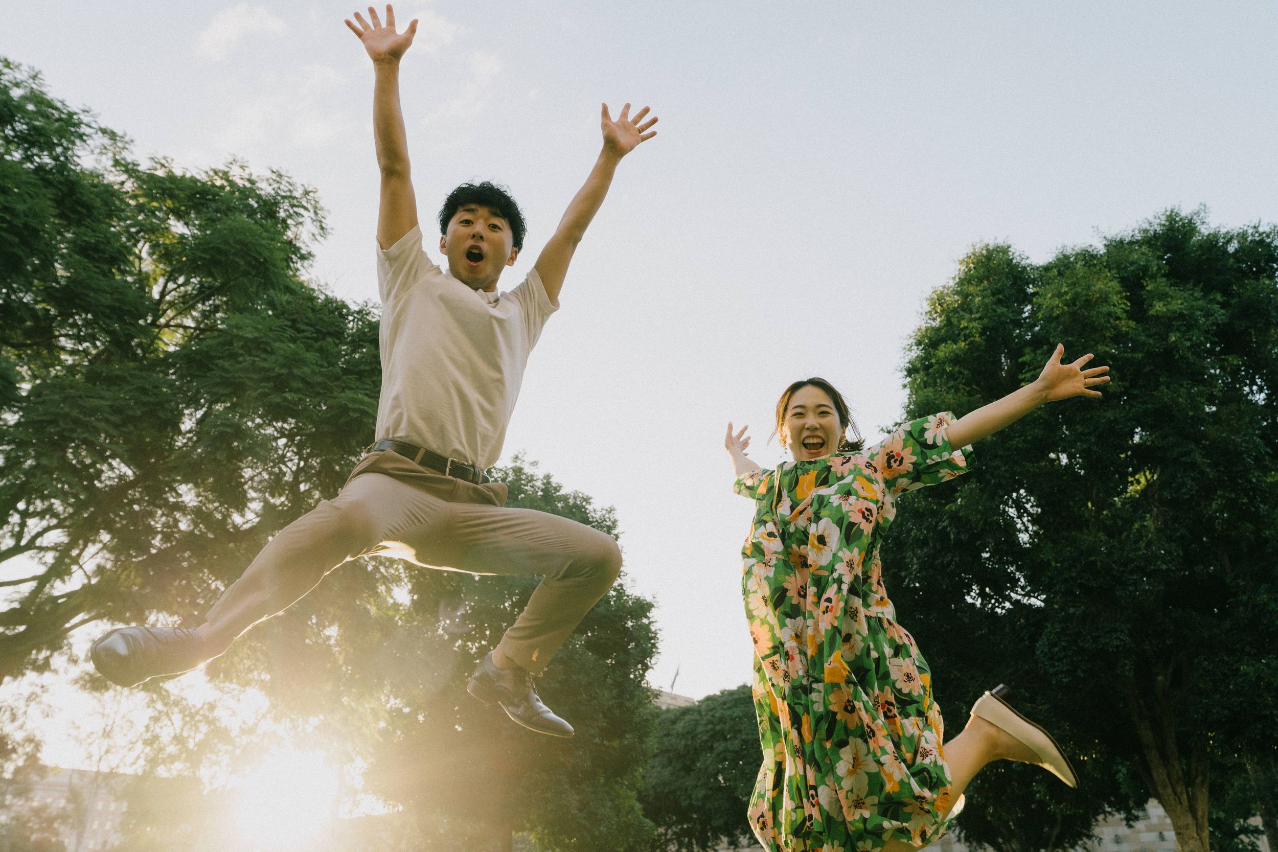 Two people joyfully jumping in the air against a sunlit forest backdrop showing pure happiness and freedom.