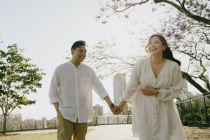 Two people walking hand in hand under cherry blossoms with city buildings in background during golden hour.