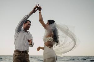 A couple dances together outdoors, with the wind dramatically flowing through the bride's white veil during sunset.