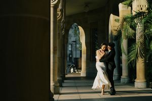 Elegant couple dancing and embracing in an archway corridor with stone columns at sunset.