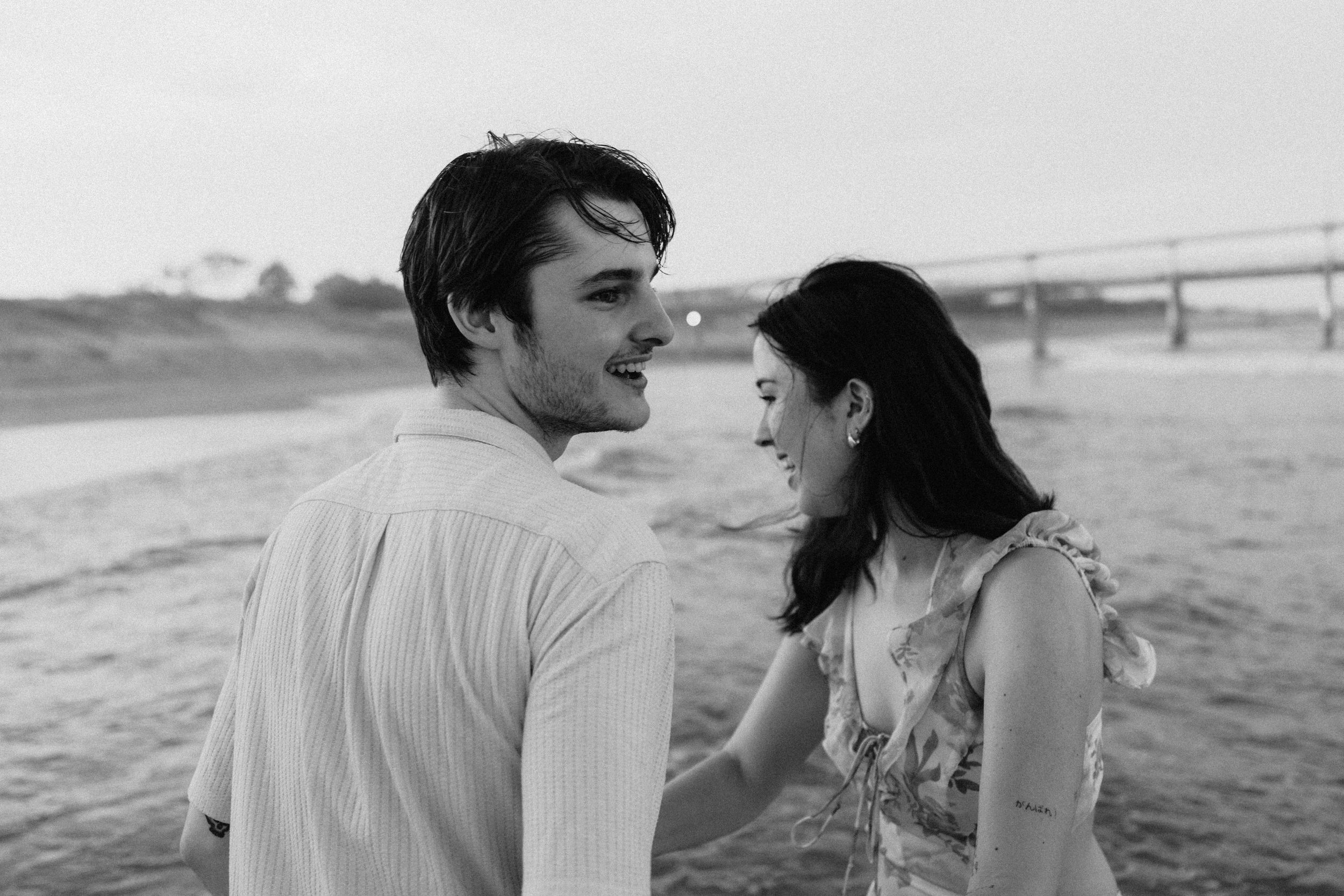 A young couple shares a romantic moment together on a beach in black and white photography.