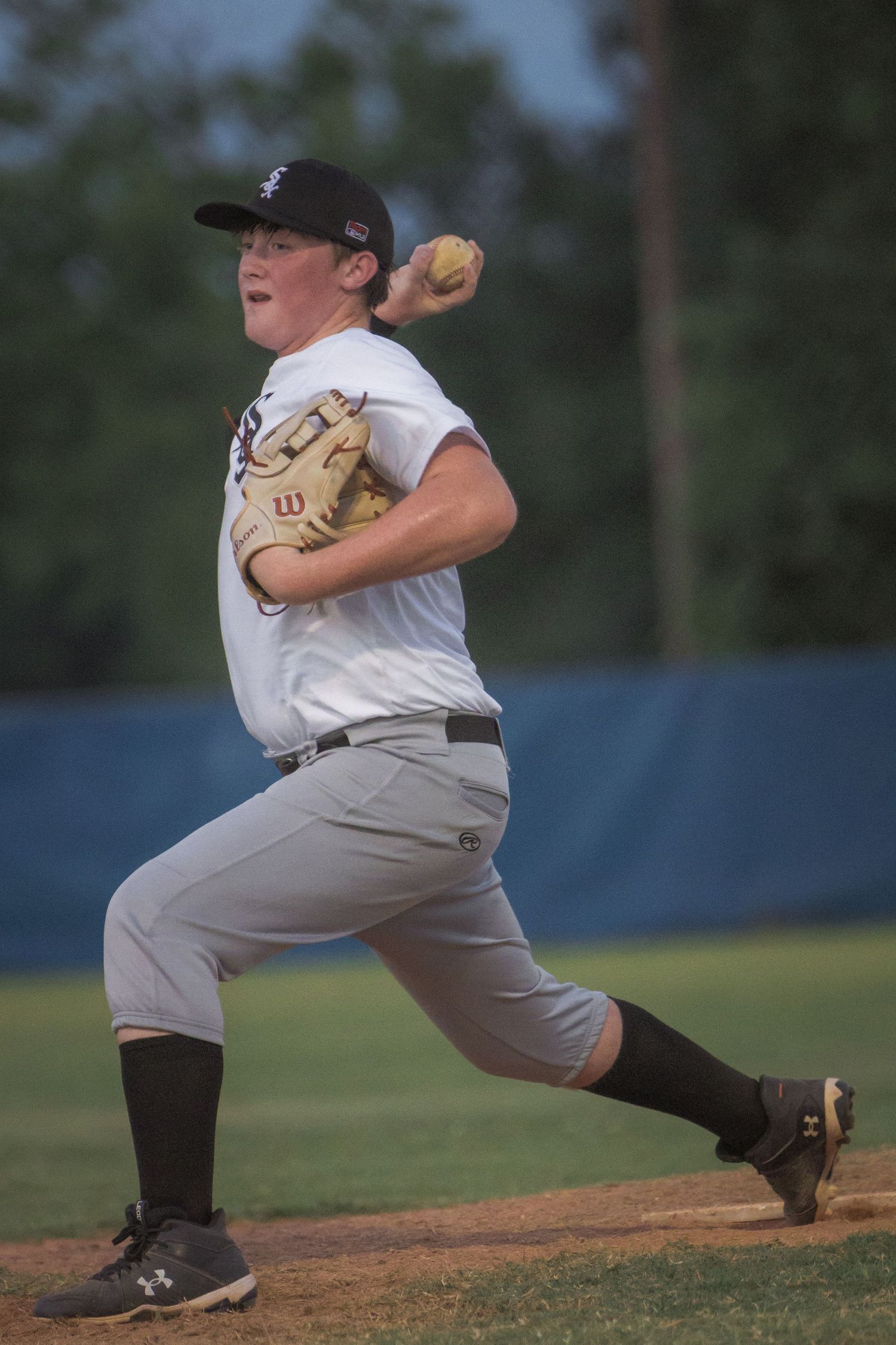 Baseball pitcher demonstrates pitching motion sequence on mound at dusk.