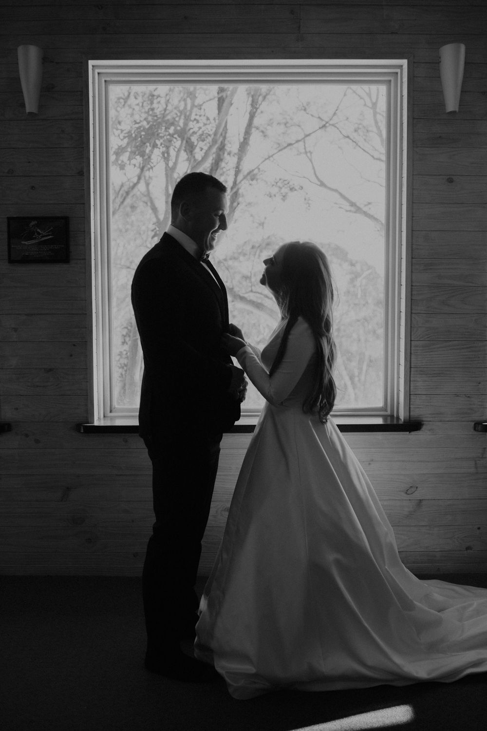 A silhouetted couple stands in romantic embrace by a bright window, creating a stunning black and white wedding moment.