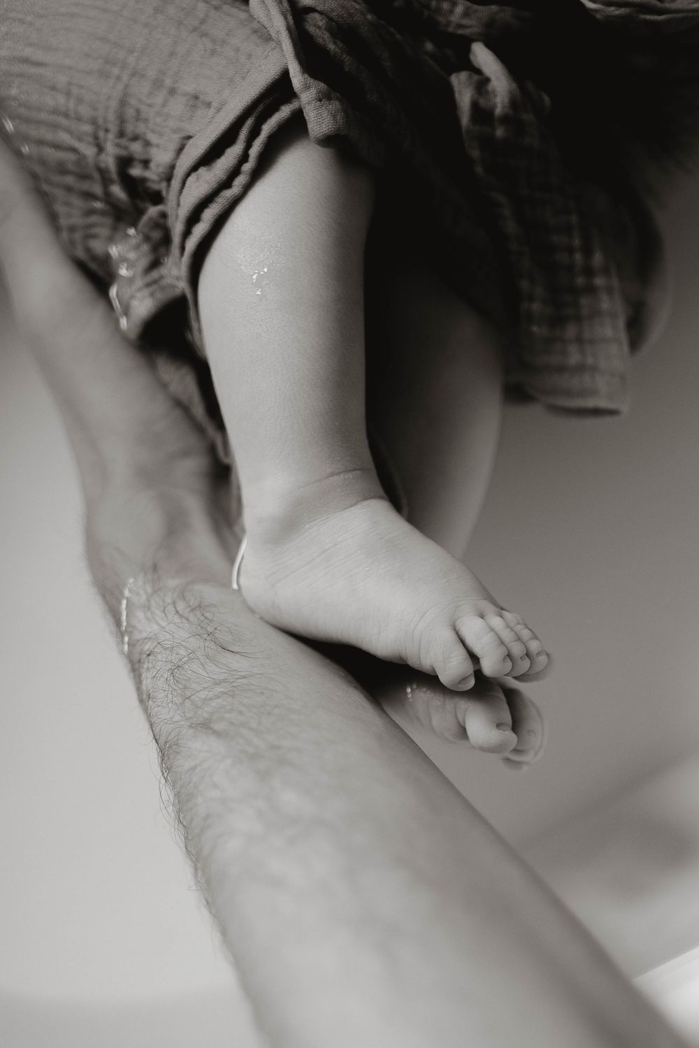 Close-up black and white photograph of an infant's tiny feet and hands against a light background.