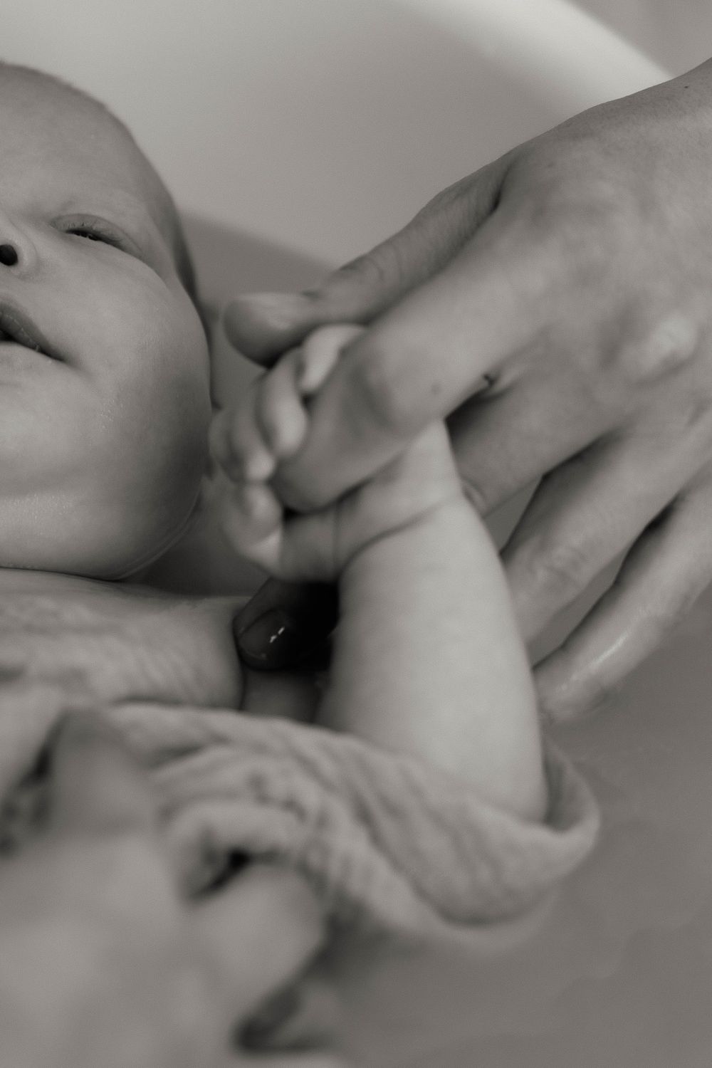 Black and white photo of a newborn baby grasping an adult's finger, symbolizing new life and parental bond.