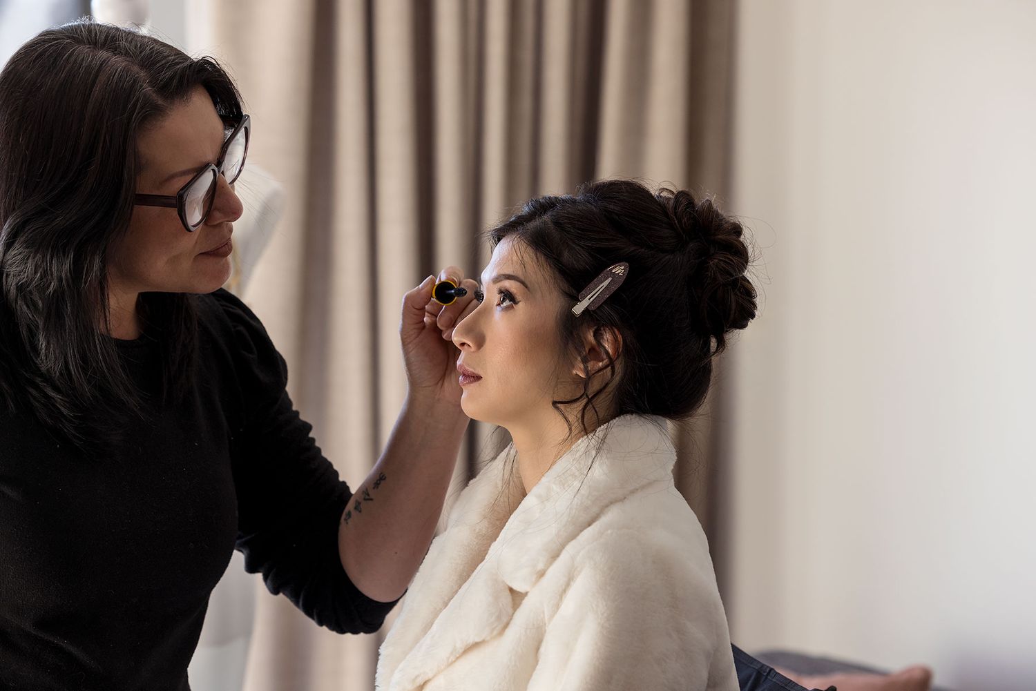 Professional makeup artist applies cosmetics to a Bride wearing a white robe in a bright hotel room setting at Quest Albury.