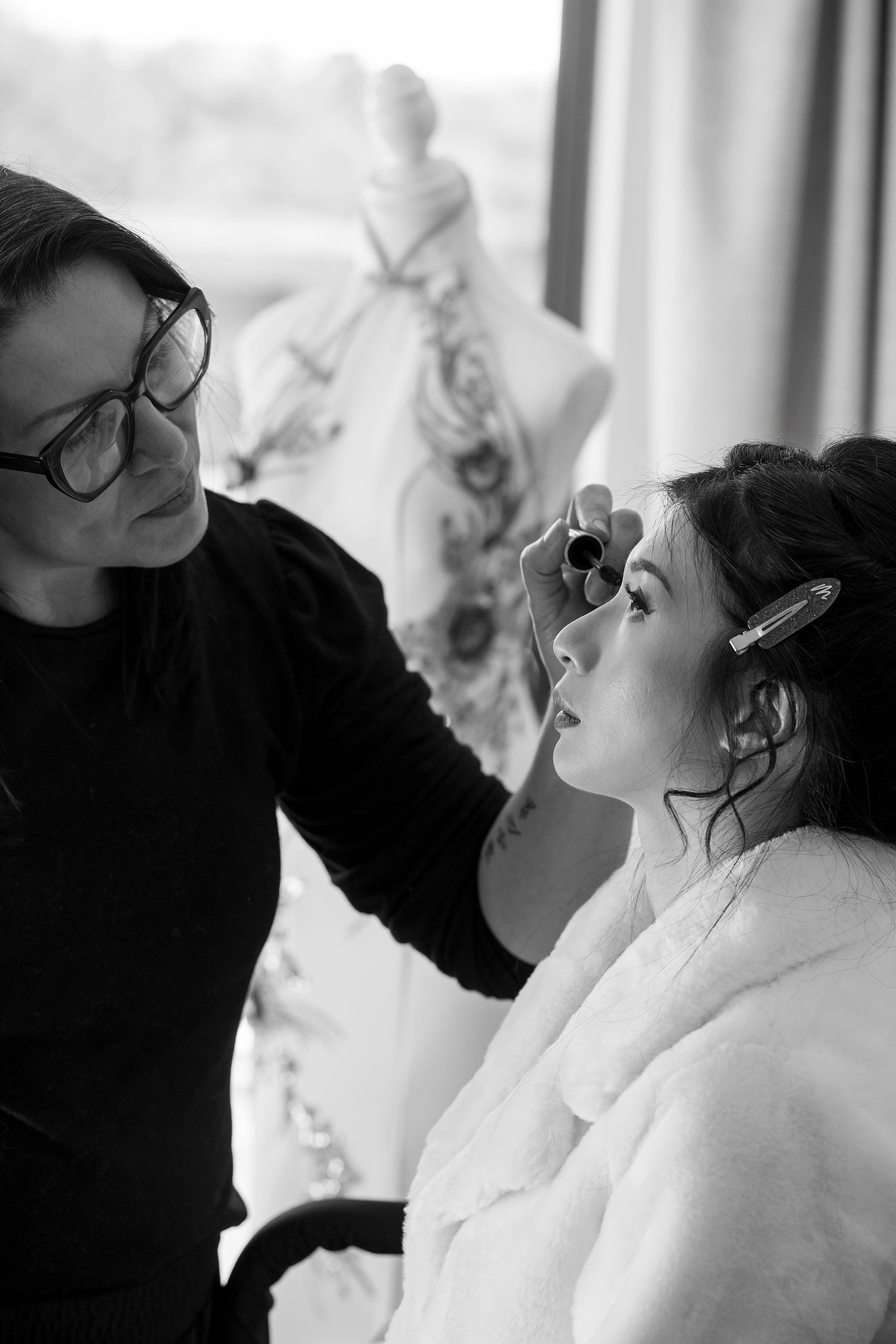 Professional makeup artist applies cosmetics to a Bride wearing a white robe in a bright hotel room setting at Quest Albury.