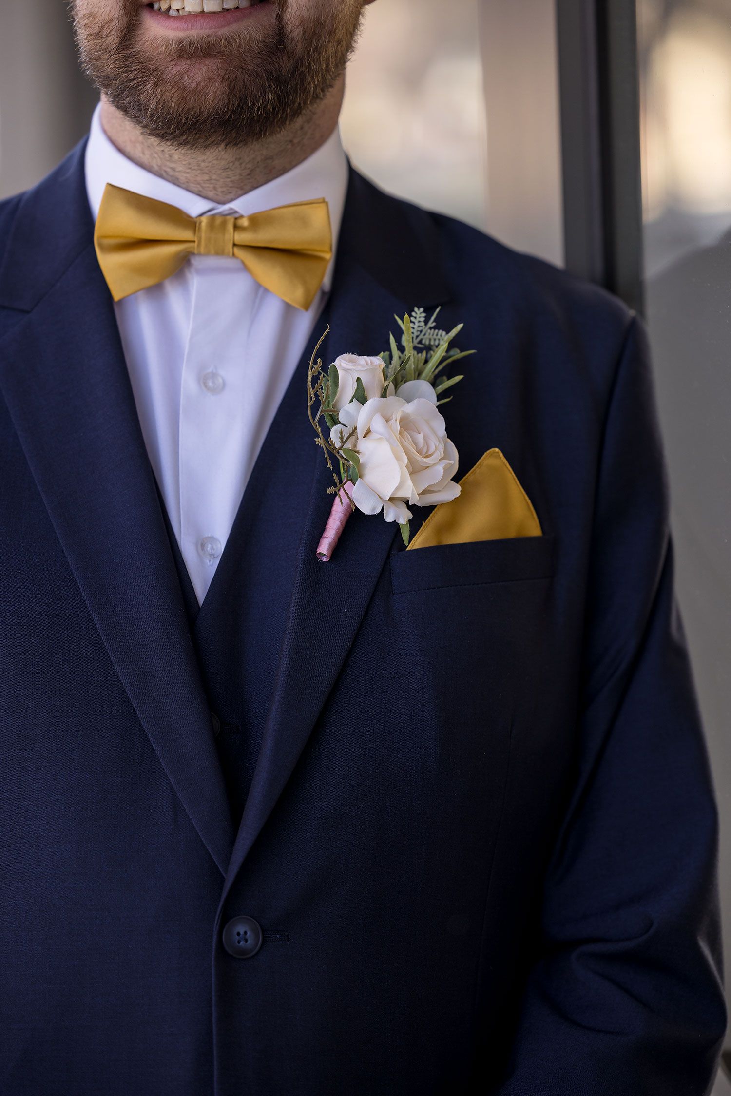 Close up of navy blue suit with mustard yellow bow tie and blush pink rose boutonniere with pocket square.