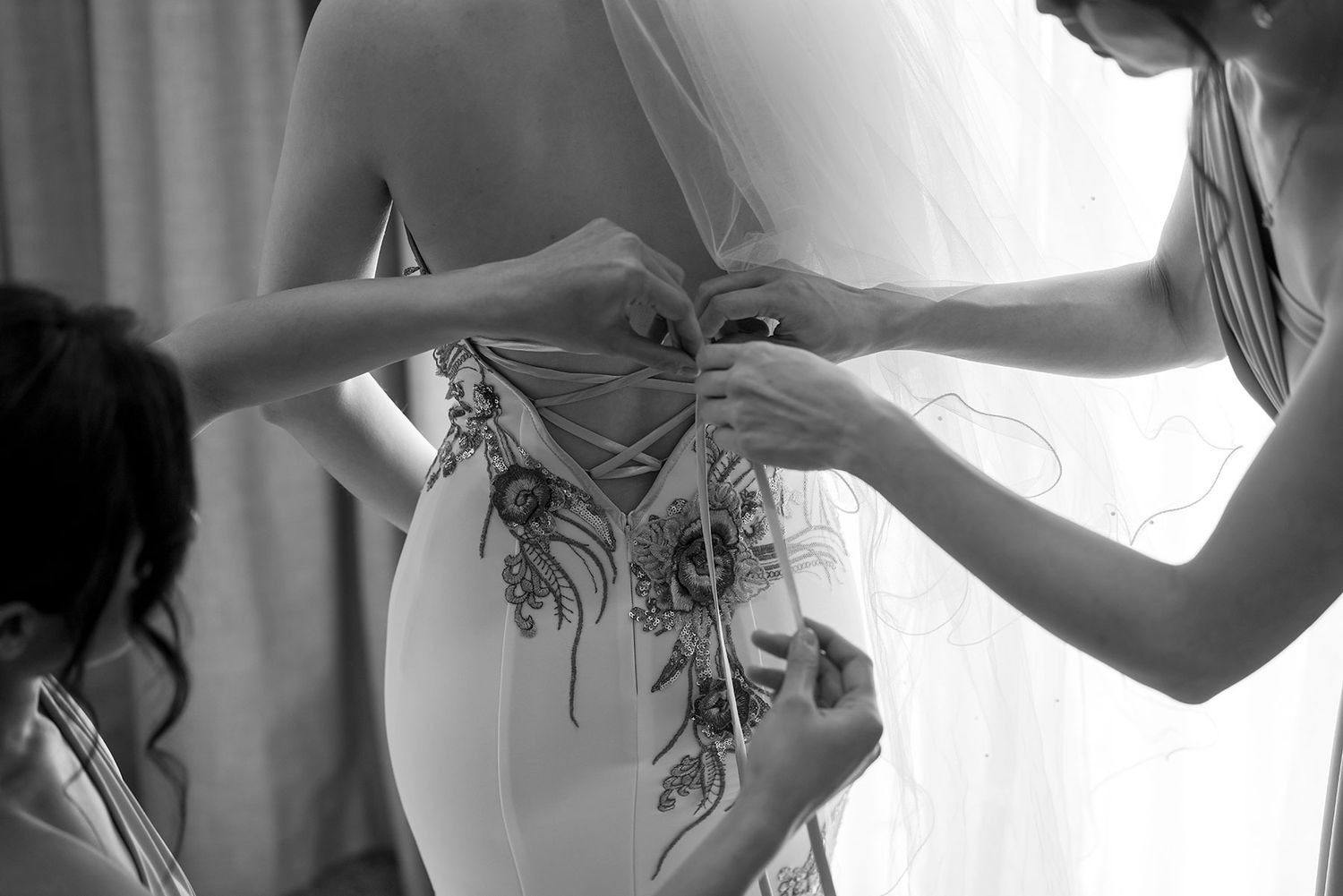 Bridesmaids help a Bride with the back of her 'East meets Dress' wedding gown at in a bright hotel room at Quest Albury.