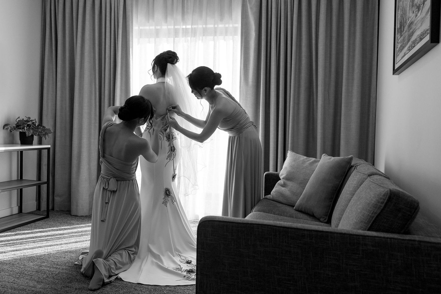 Bridesmaids help a Bride with the back of her 'East meets Dress' wedding gown at in a bright hotel room at Quest Albury.