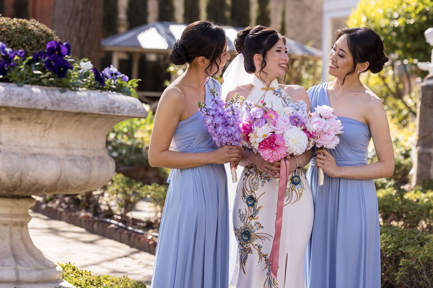 Wedding party in periwinkle blue dresses pose together in a garden with pink and white floral bouquets at St. Matthews Church.