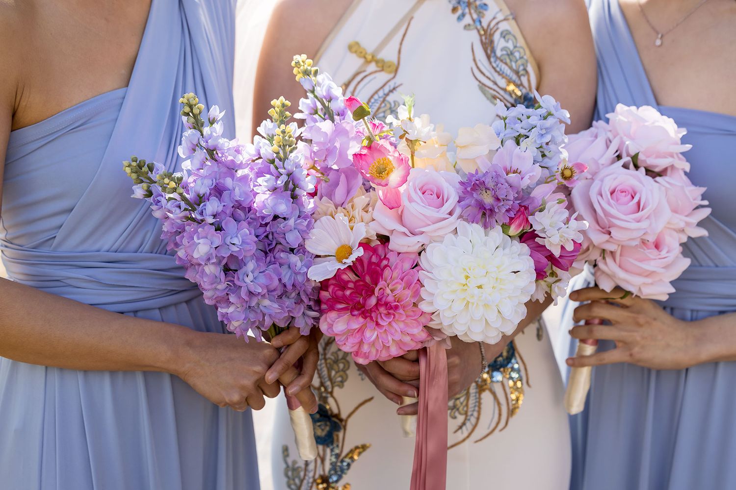 Bridesmaids in light blue dresses holding stunning bouquets of pink, purple and white flowers with silk ribbons.