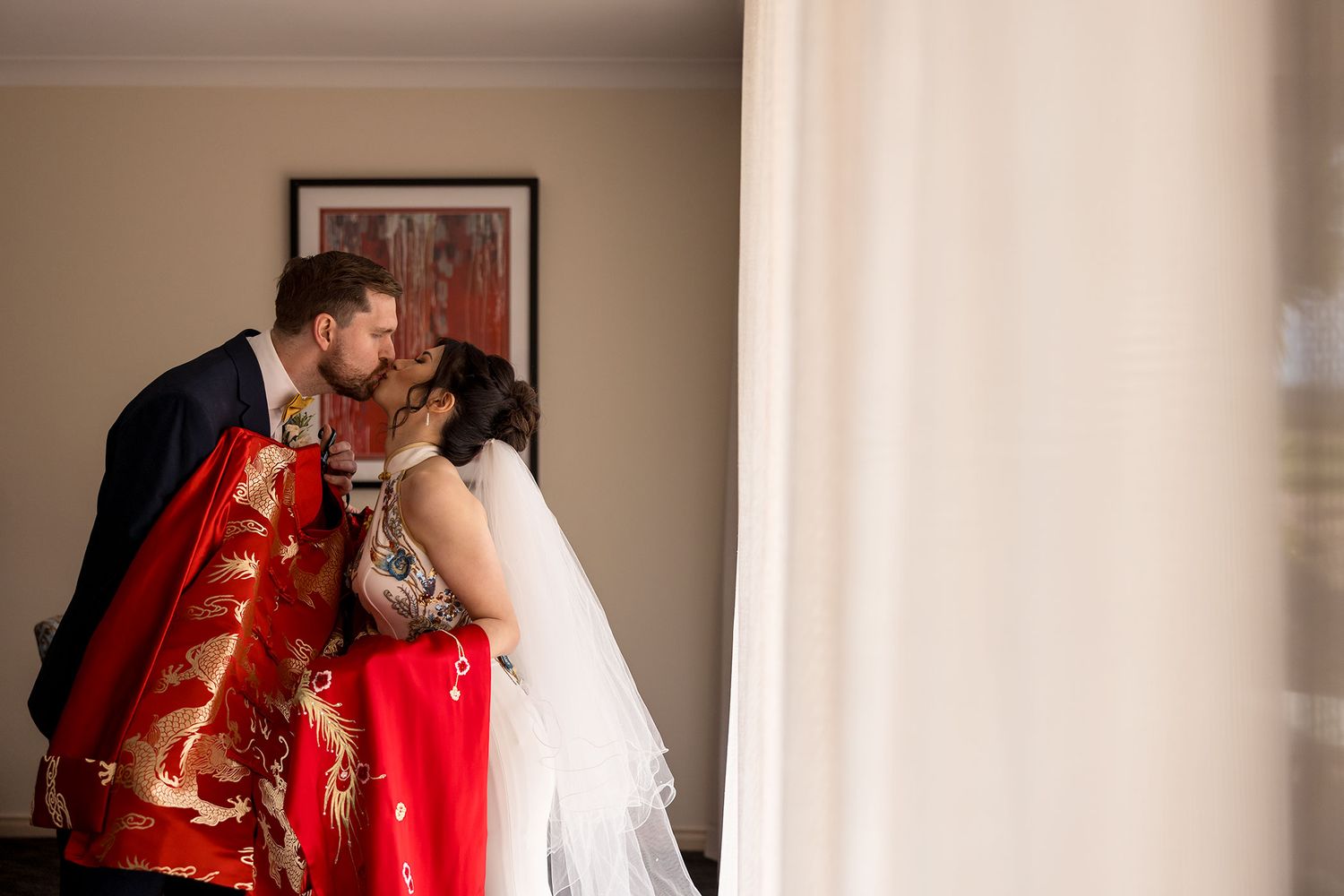 A couple shares a kiss in wedding attire, with the bride in white and red traditional Chinese dress at De Bortoli Rutherglen Estate.