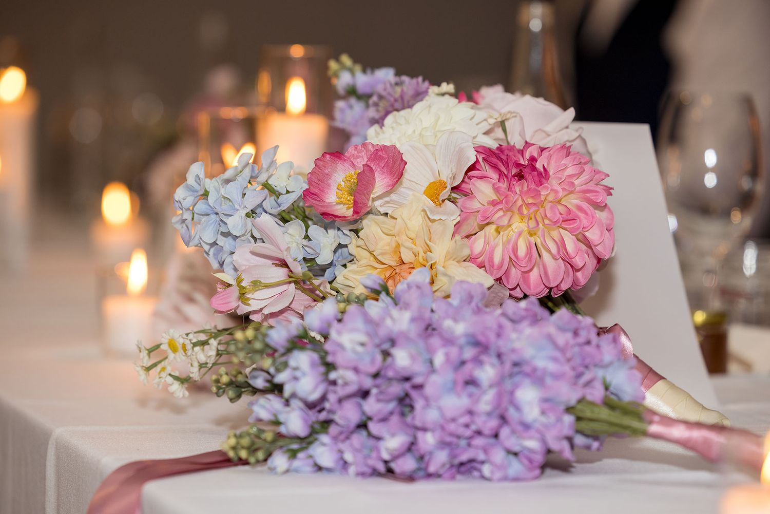 A romantic floral centerpiece with pink dahlias, purple hydrangeas and candles glowing softly in the background.