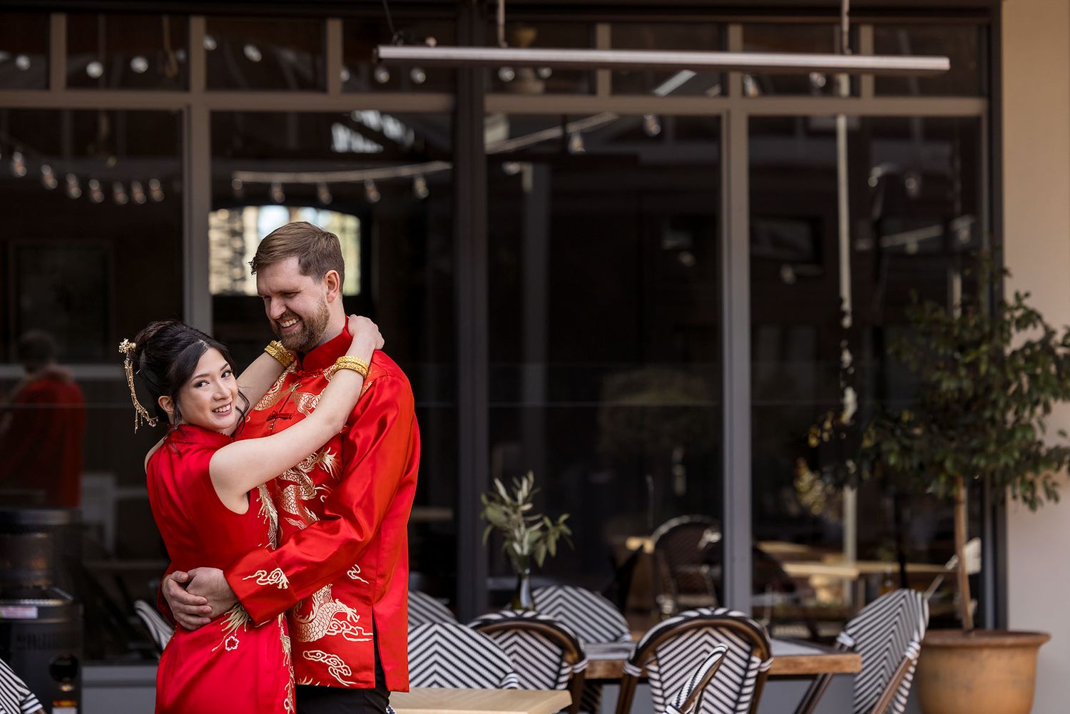 A couple in matching red coats share an intimate moment leaning against a concrete wall at sunset.