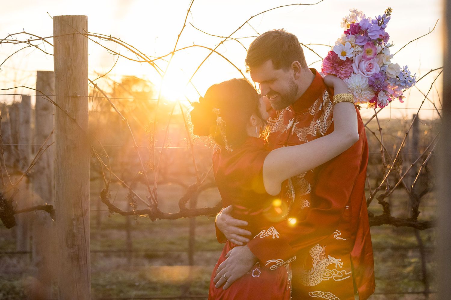 Romantic Bride and Groom embracing in the vineyard at sunset while holding brightly colored wedding flowers at De Bortoli Rutherglen Estate.
