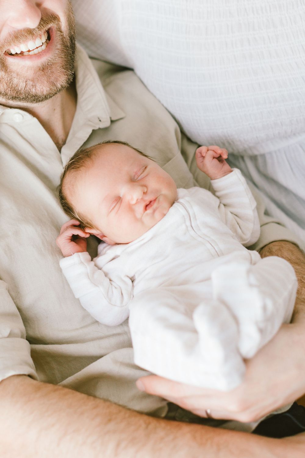 Sleeping newborn in white onesie resting peacefully on parent's chest.