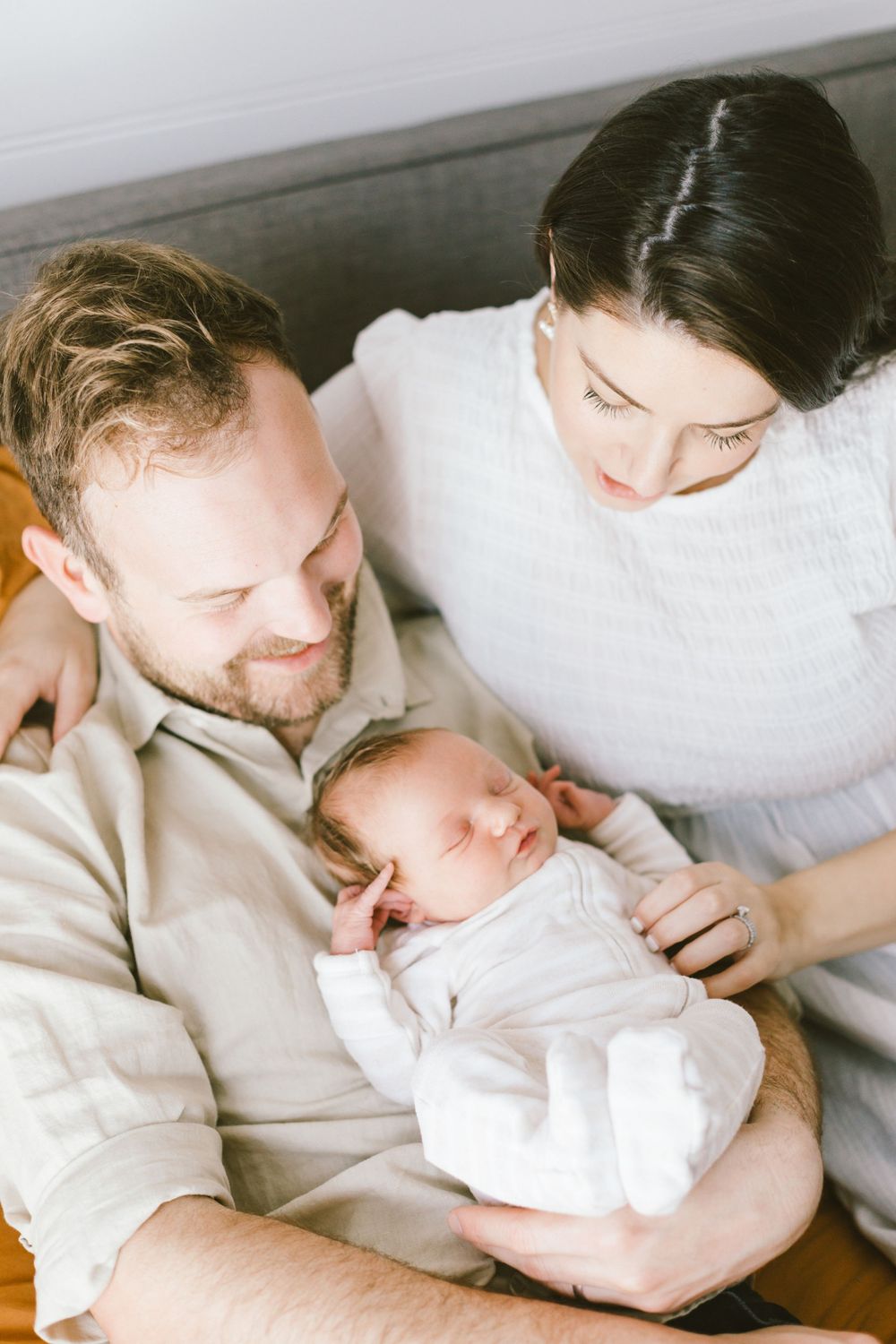 Intimate family moment with sleeping newborn baby in white clothes.