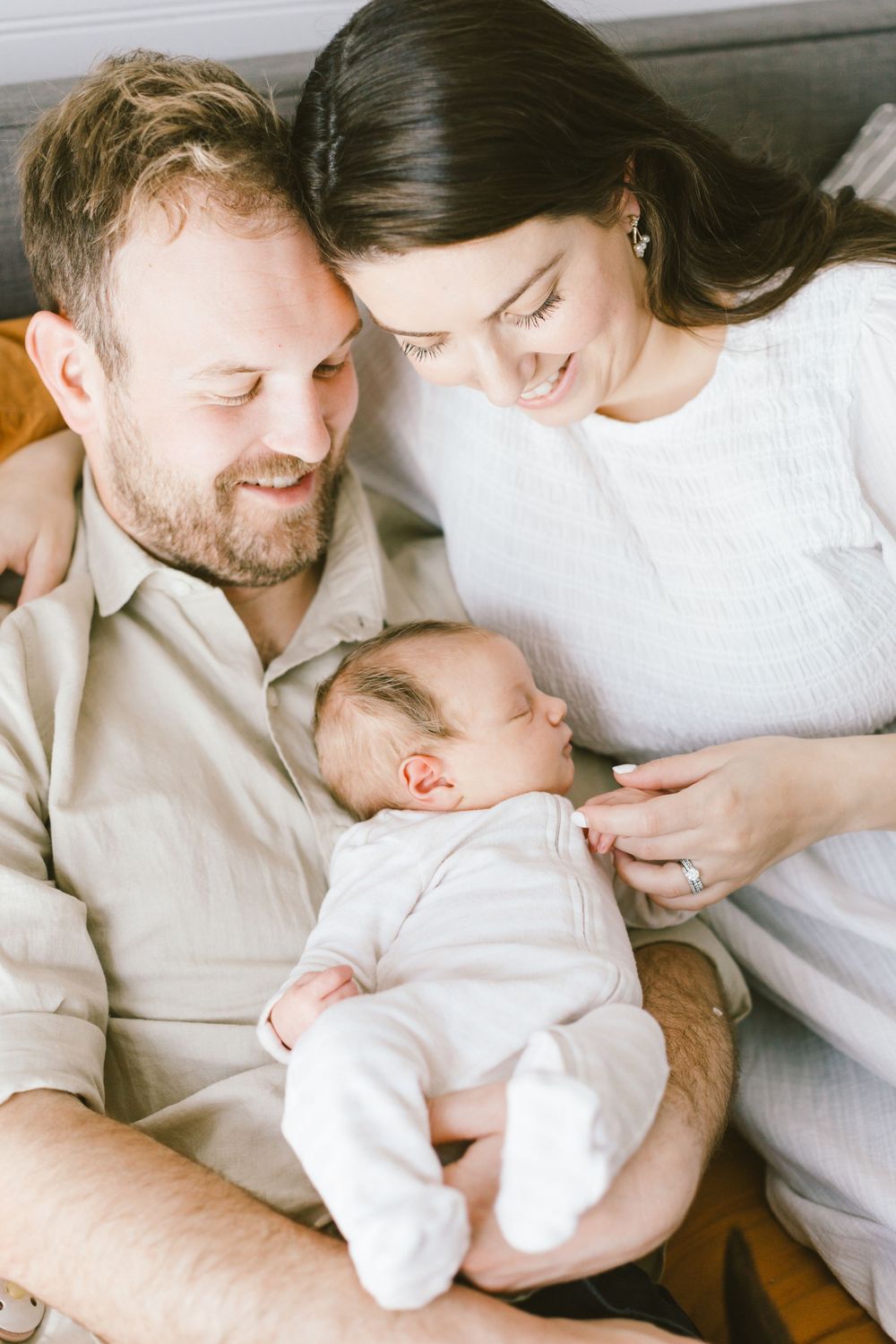 Sweet family moment with sleeping newborn baby in white outfit.