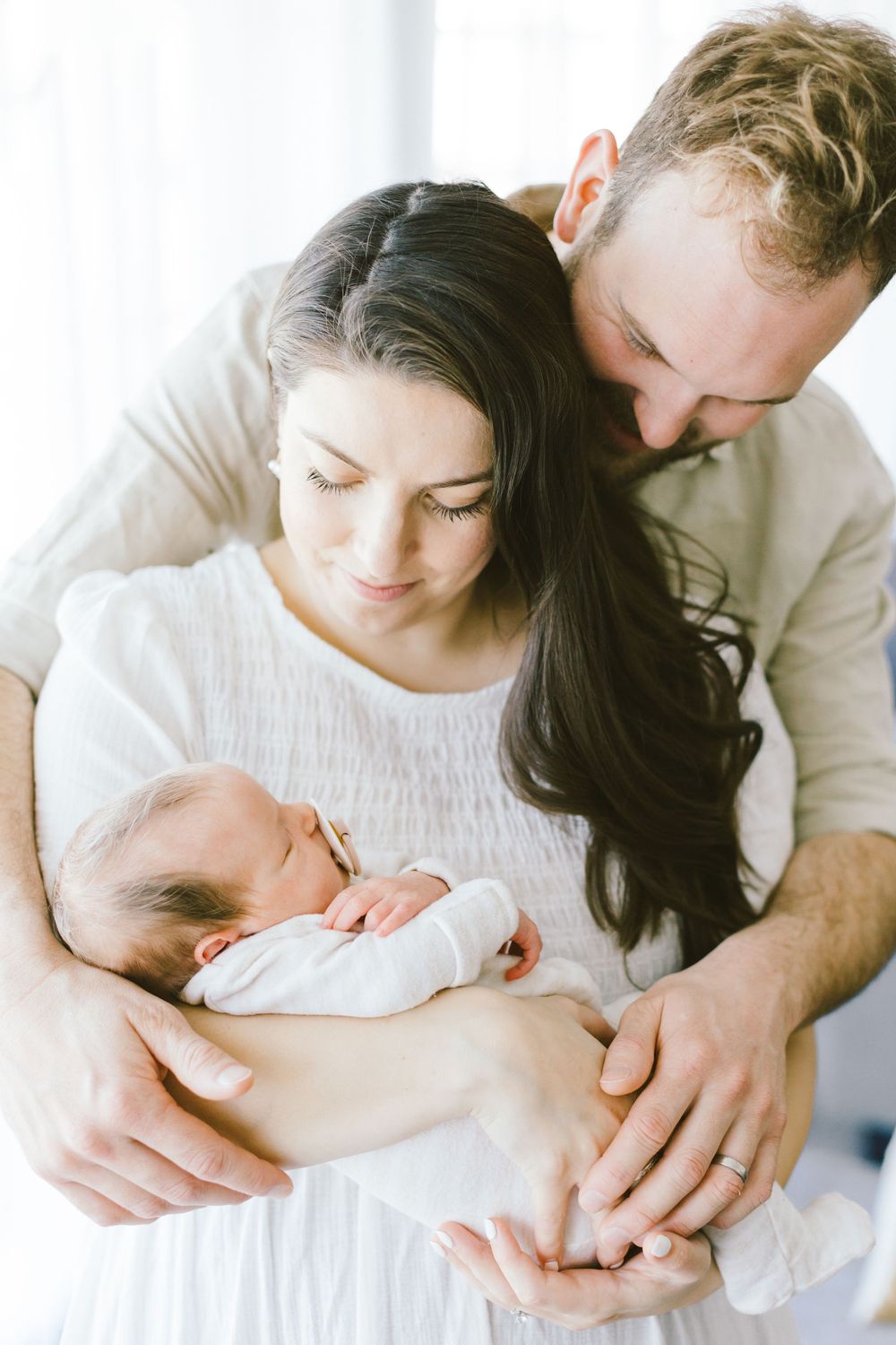 Intimate family moment as parents cuddle with their newborn baby in white clothing.