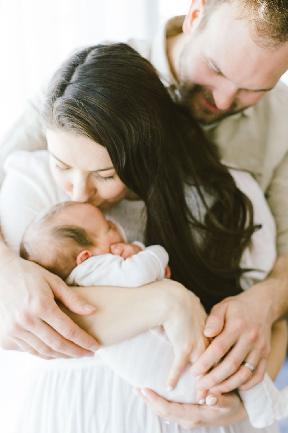 Parents share tender moment while holding their sleeping newborn baby close.