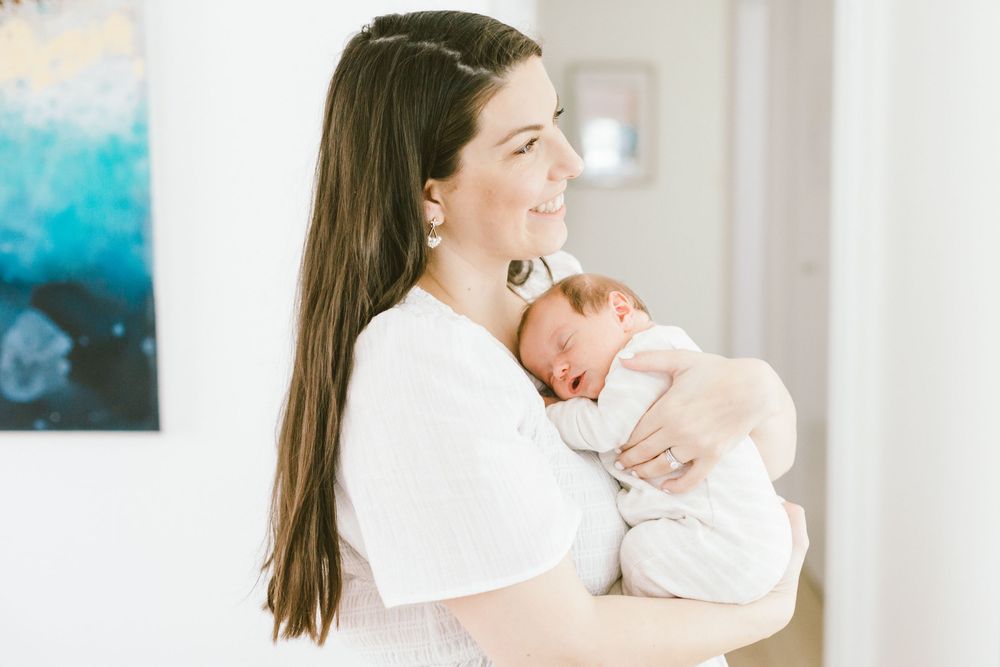 Person in white holds sleeping newborn baby against colorful wall art background.
