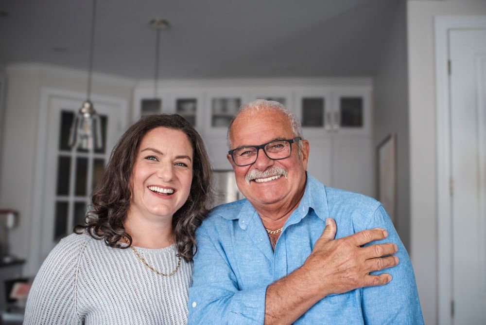 Father and daughter stand together smiling happily in the kitchen.