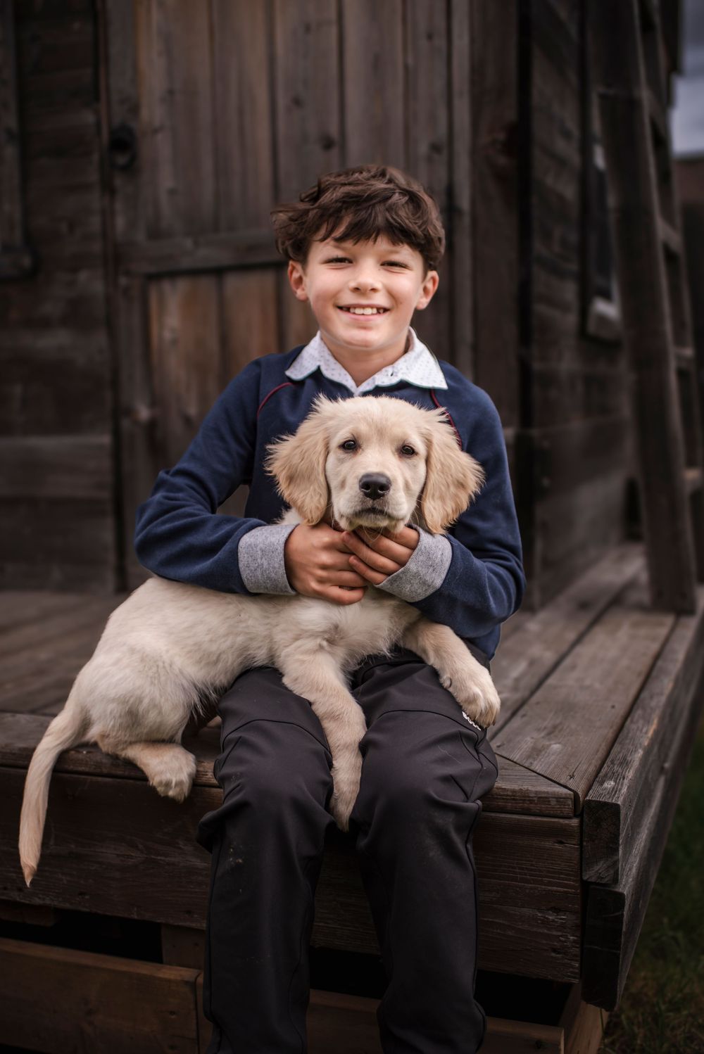 A boy sits on the deck of his playhouse and holds his new puppy.