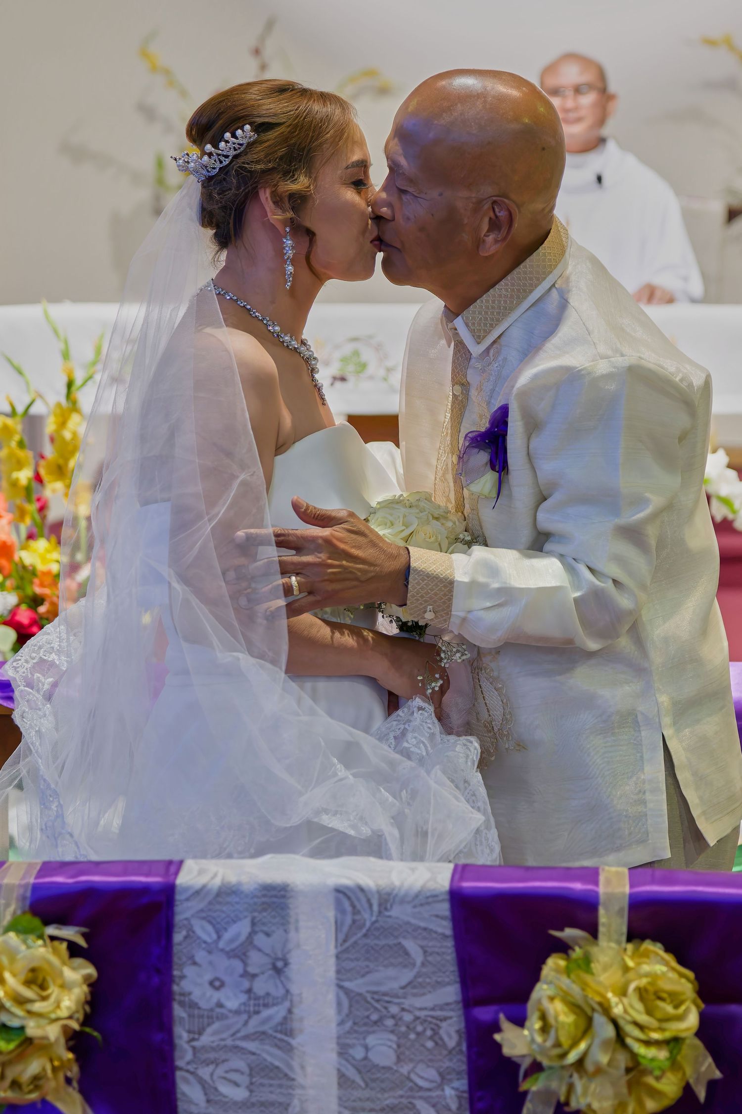 A traditional wedding ceremony takes place in a church with people in formal attire including white barongs and a bridal gown.