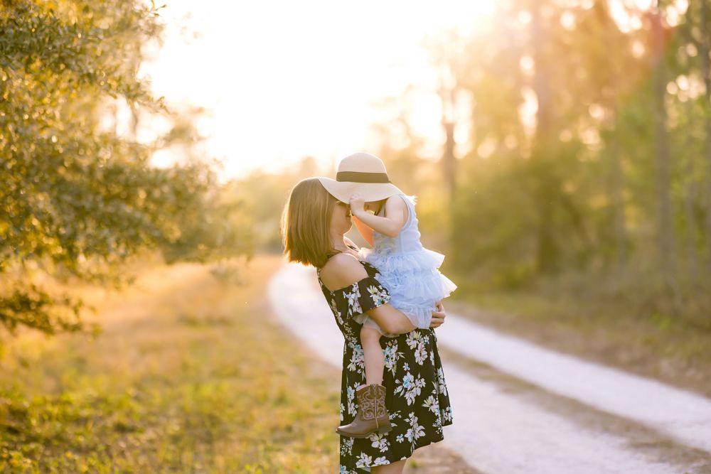 A heartwarming sunset portrait showing a floral dress and white lace dress against a golden forest backdrop. Photos by Tampa Photographer Di