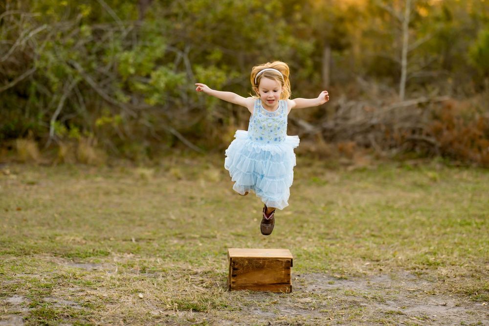 A joyful leap over a wooden crate captured in a whimsical outdoor portrait. Photos by Tampa Photographer DigitalMyst Photography