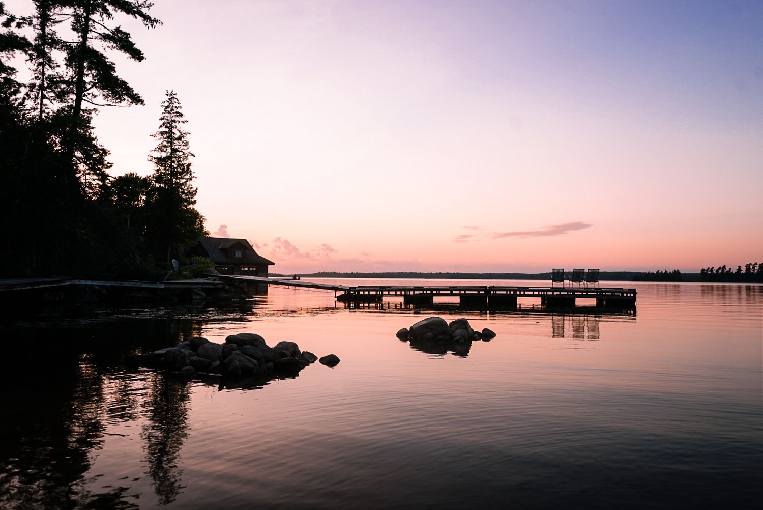 Serene sunset over calm lake waters with silhouetted trees and docks.