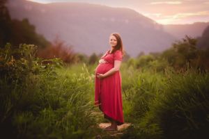 Pregnant woman standing in tall grass at sunset, photographed by Urso Photography.