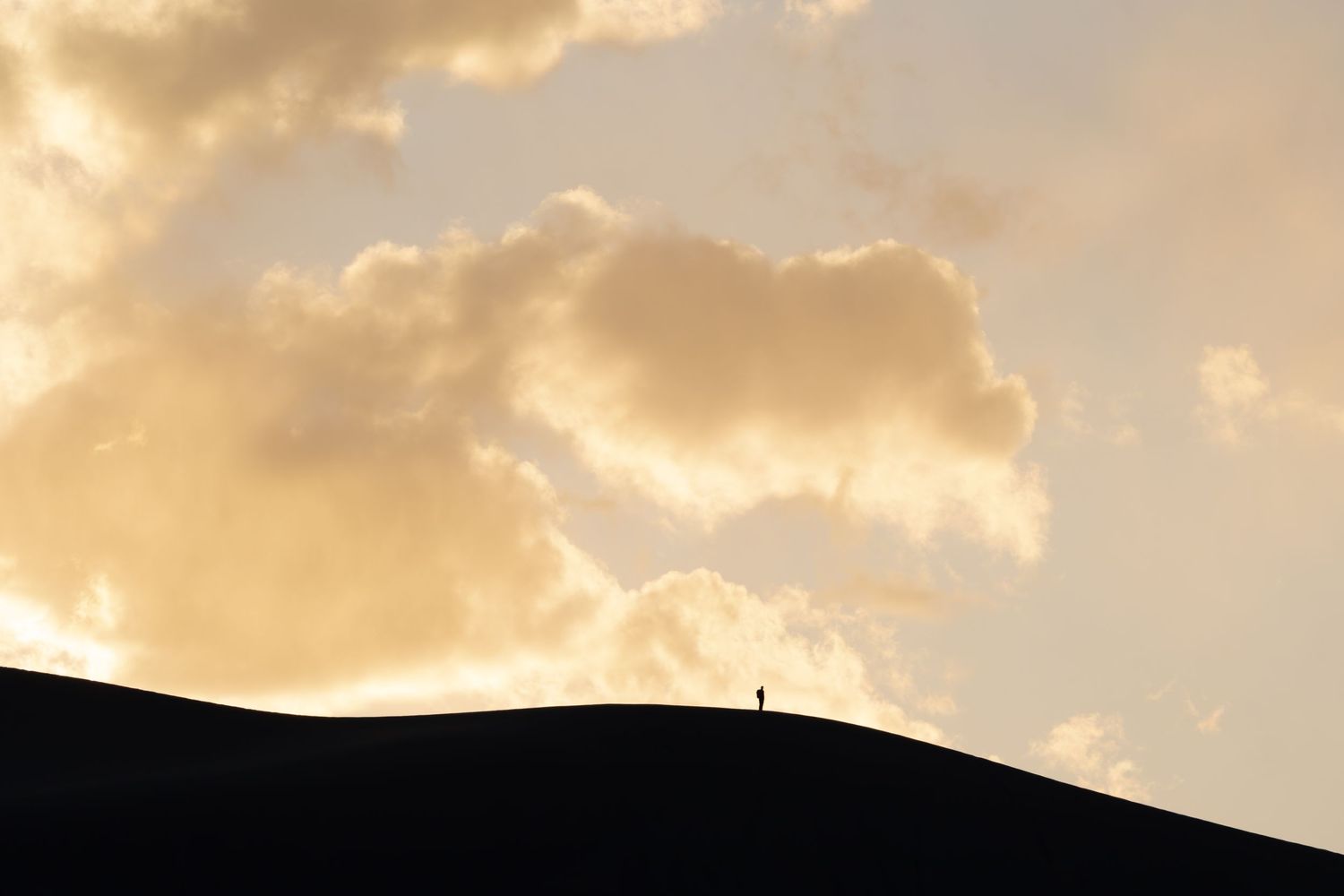 Tiny silhouette of person standing on sand dune against dramatic sunset sky. Great sand dunes national park