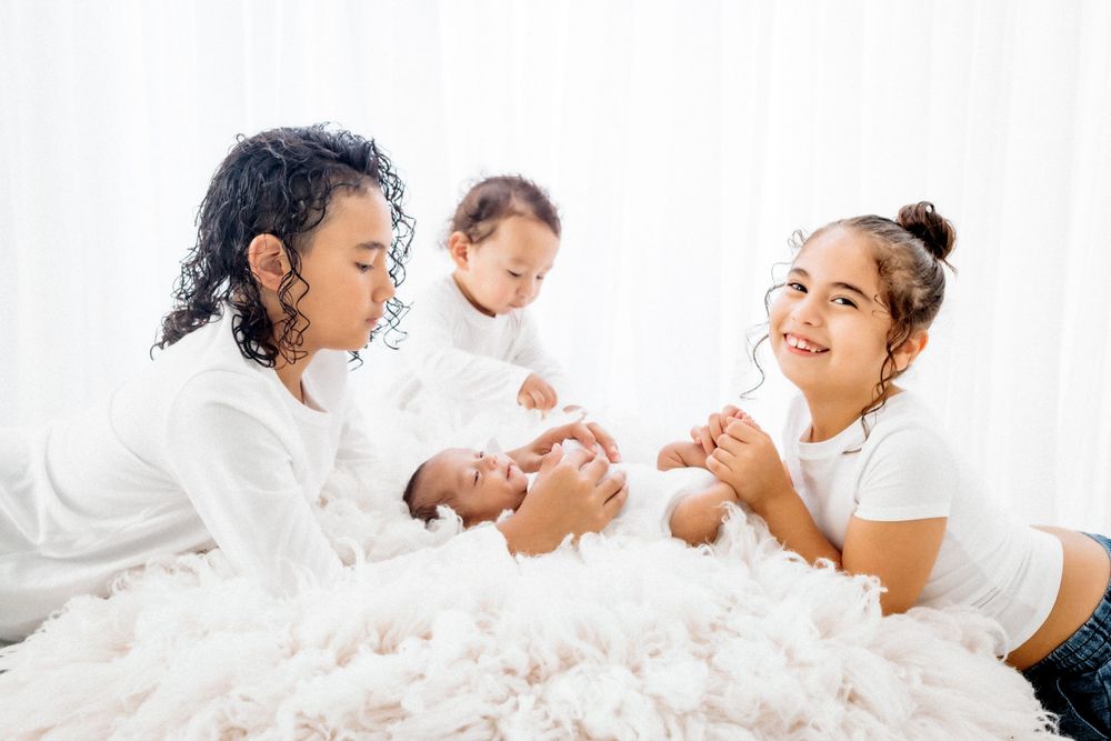 Happy diverse children lie on cozy white bedding having fun together during playtime at home.