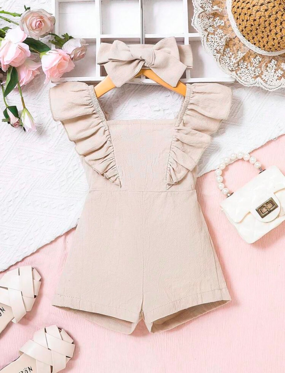 Beige ruffled romper for children displayed on pink background with floral accents.