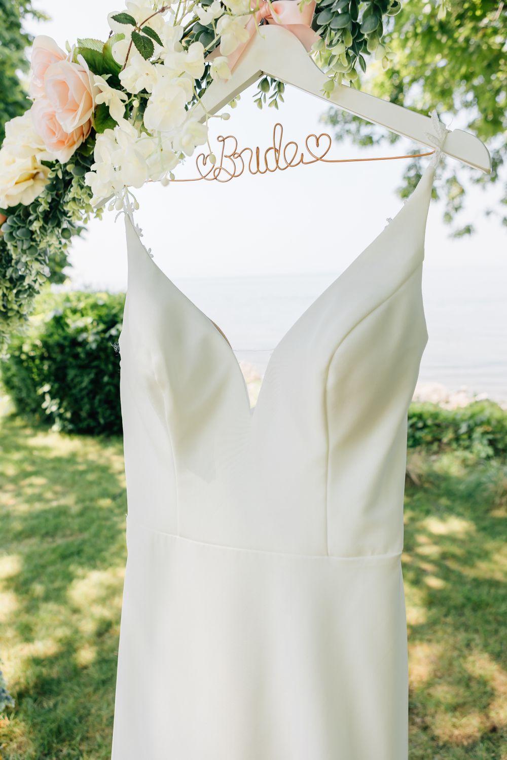 An elegant white wedding dress hanging from a custom hanger with floral decorations.