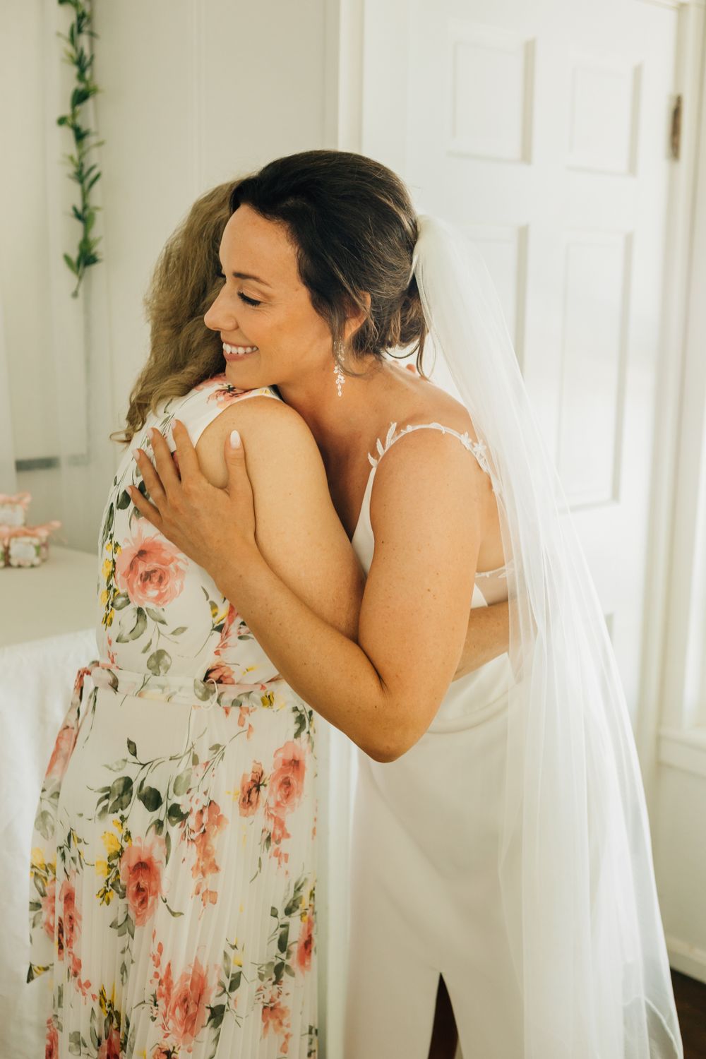 Two figures sharing an emotional embrace while wearing floral and white dresses.