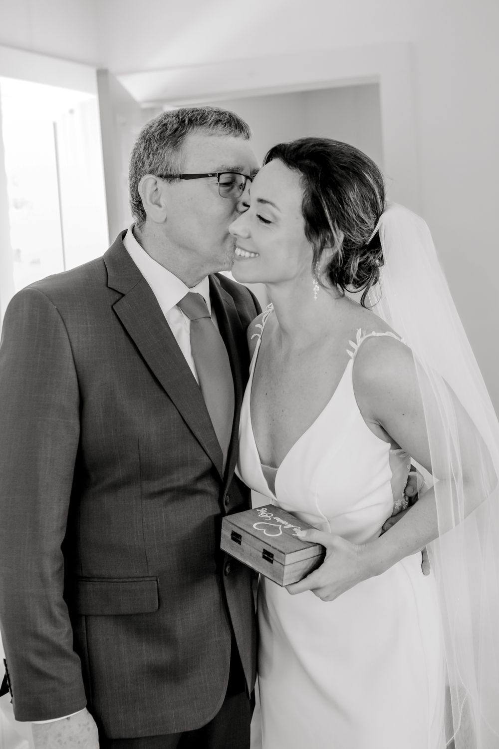 A wedding couple sharing a tender moment against a white wall.
