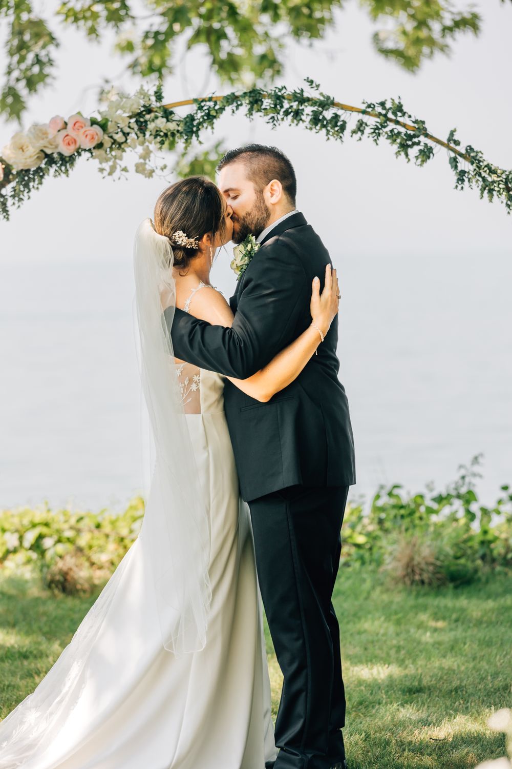 Newlyweds sharing their first kiss under a natural green arch outdoors.