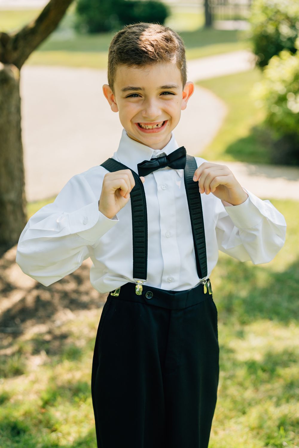 Young ring bearer in formal black and white attire adjusting his suspenders.