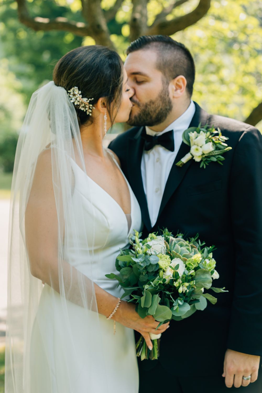 Bride and groom sharing an intimate moment while holding a green and white bouquet.