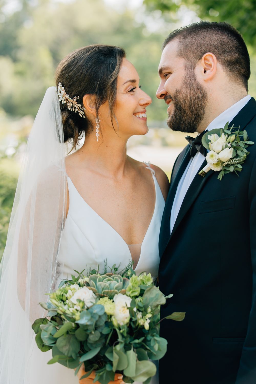 A romantic wedding couple in a garden setting with the bride holding a white and green bouquet.