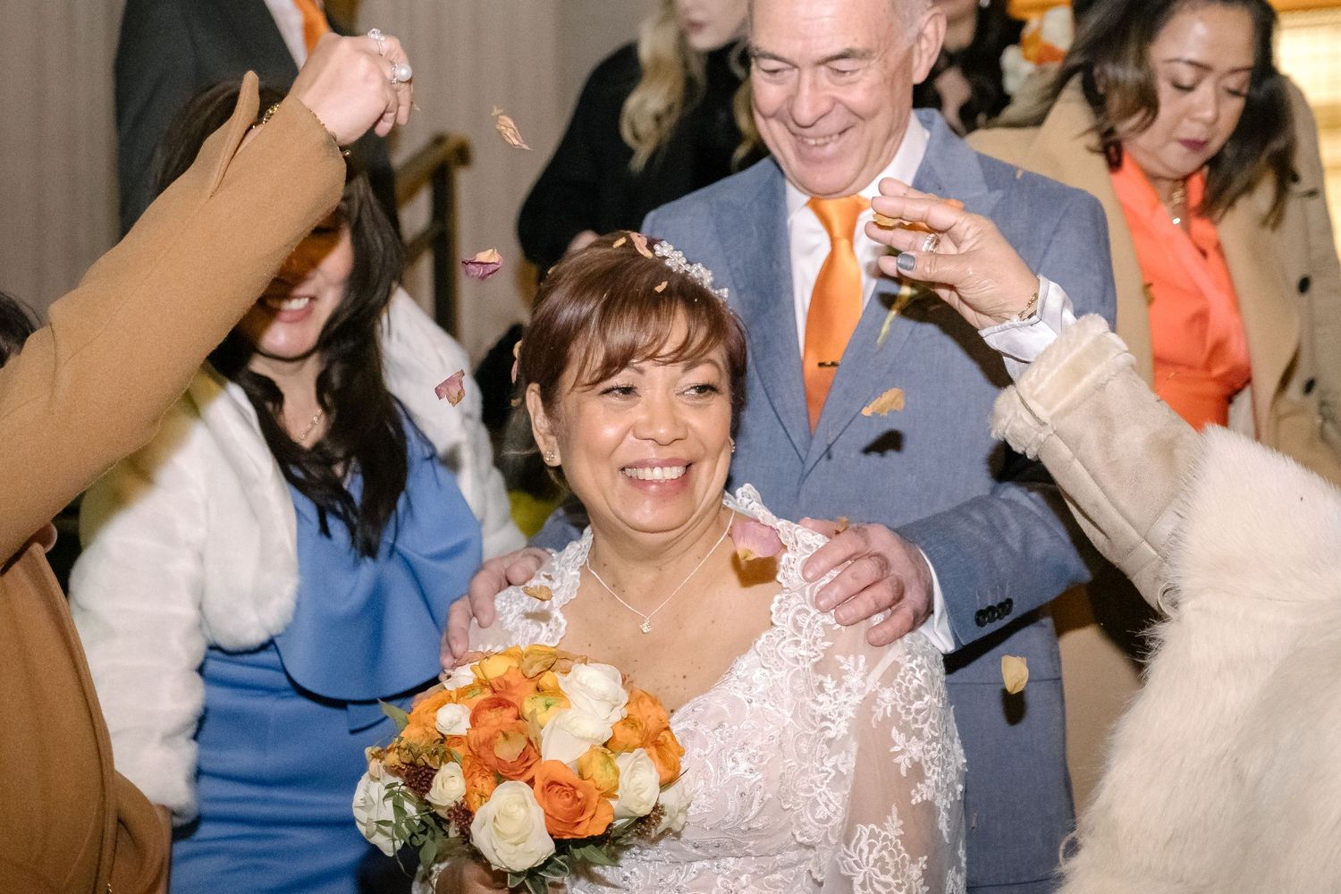 A joyous wedding celebration with people dancing as the happy couple holds bouquets of orange and white flowers.