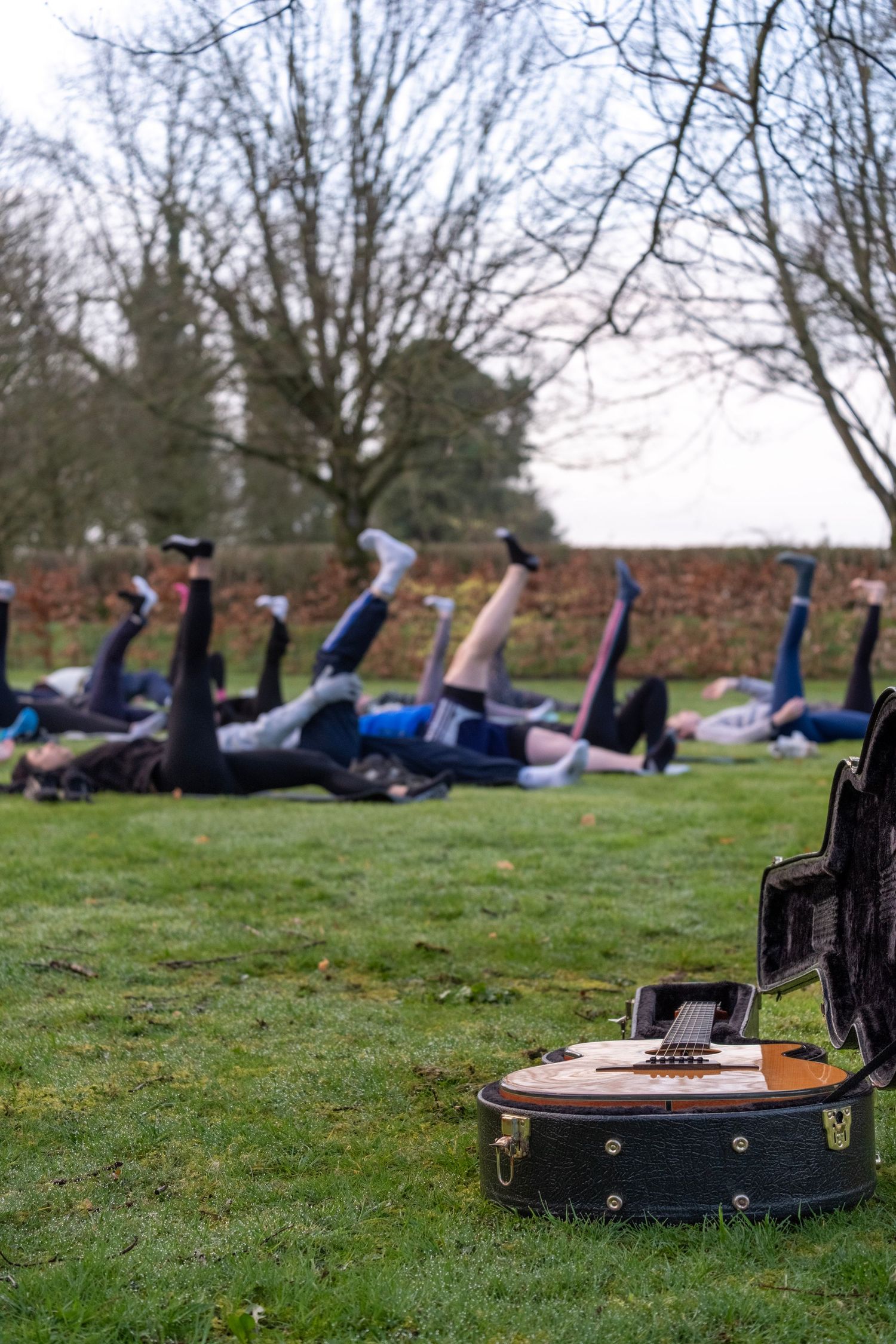 Group fitness class lying on ground with legs raised, vintage suitcase with guitar in foreground.
Kildare, Ireland.