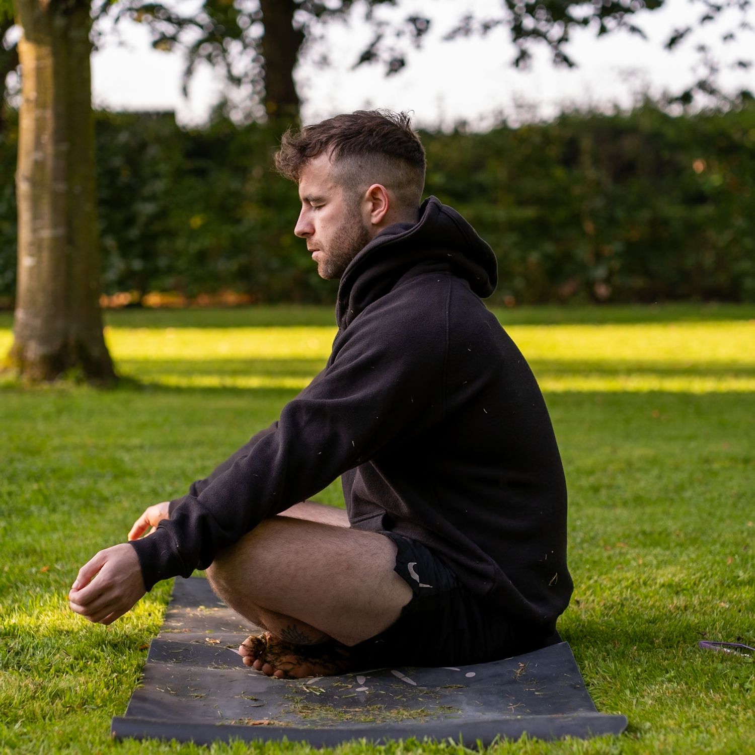 Person in black hoodie sitting in meditation pose on yoga mat in grassy park.
Kildare, Ireland.