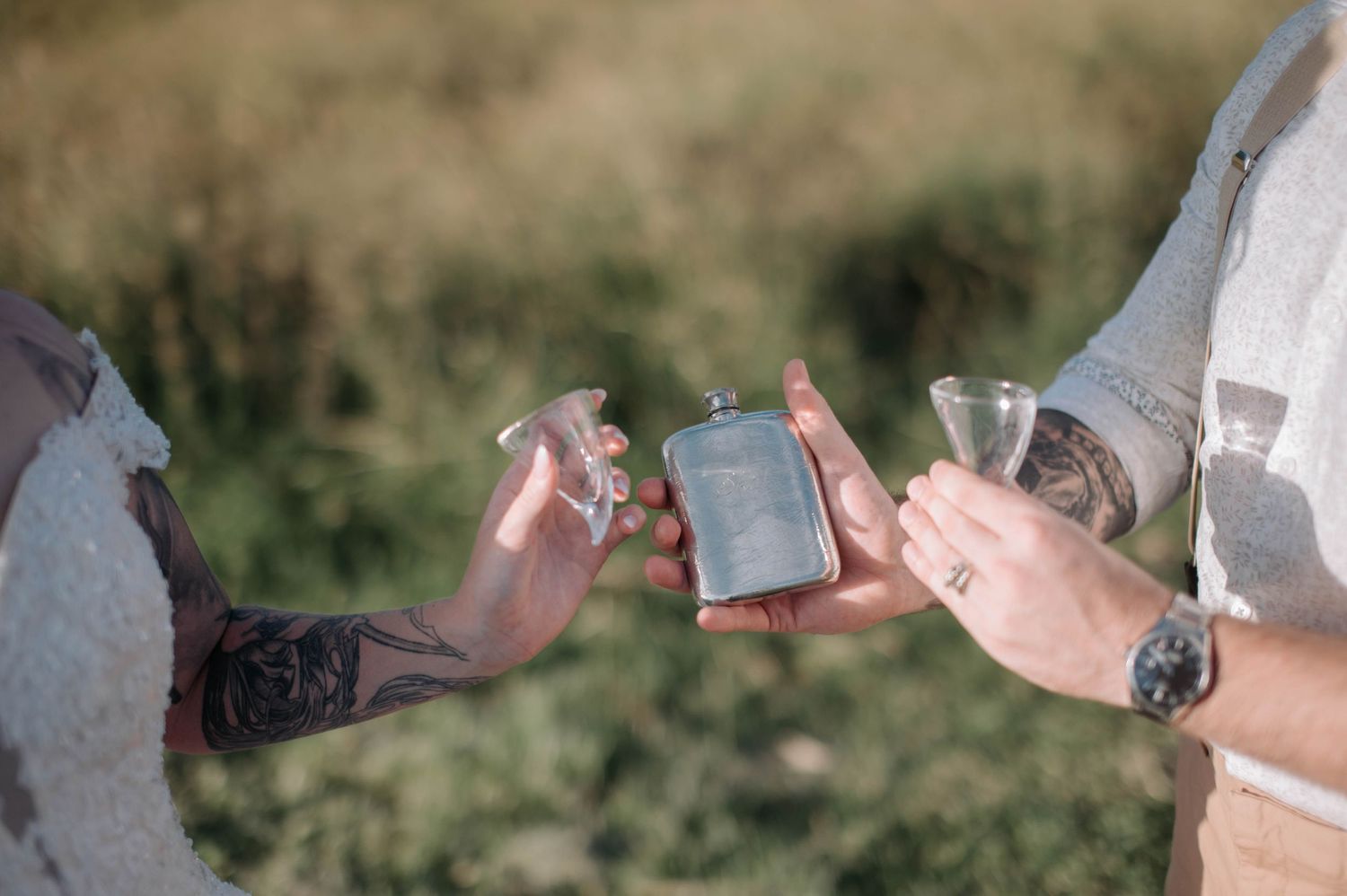Hands holding shot glasses during outdoor wedding celebration.