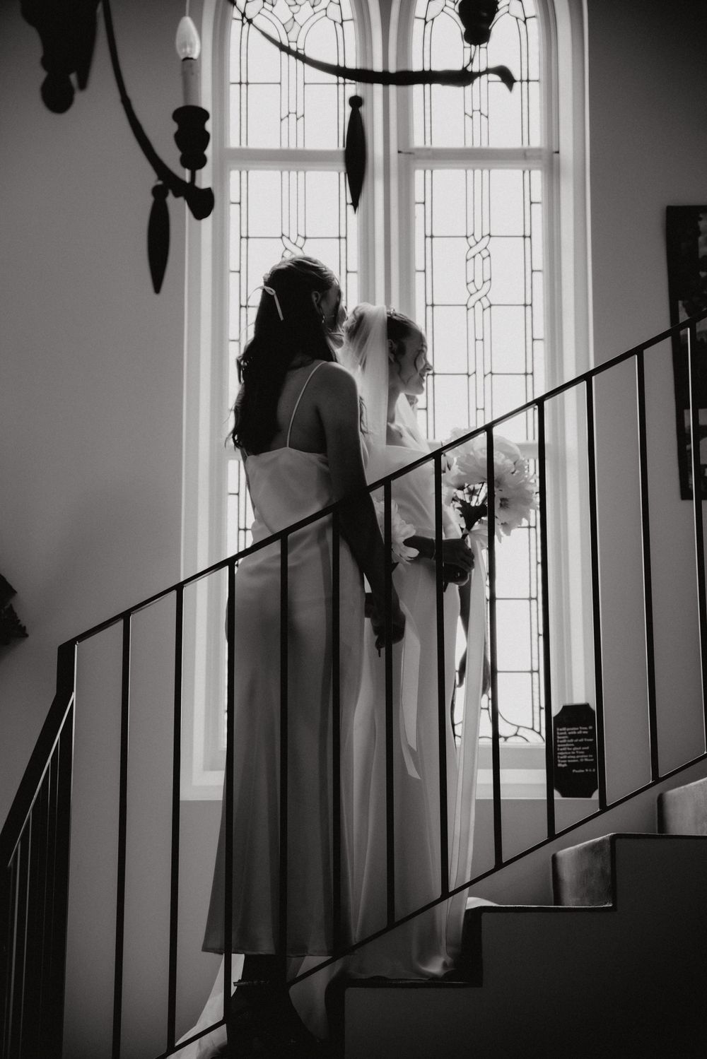 Black and white photo of two people on staircase near stained glass window.