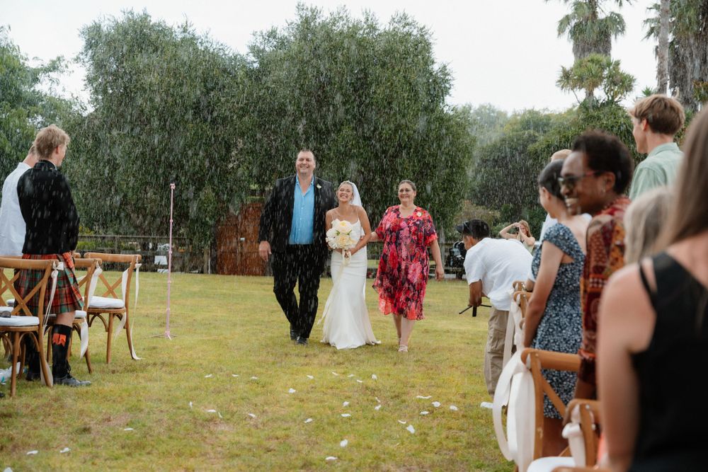 Wedding guests gather outdoors on a grassy lawn with scattered flower petals during an intimate garden ceremony.