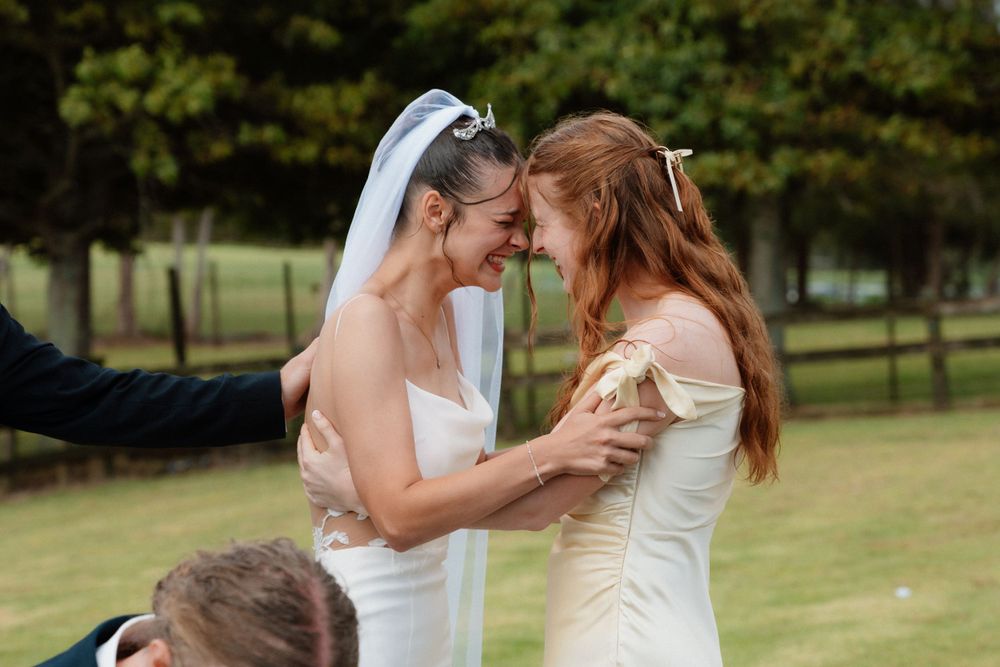 Two people in white wedding dresses share an intimate moment together on a grassy lawn during their wedding celebration.